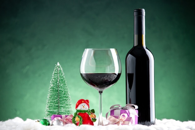 緑の背景に正面図のワイングラスとボトルの小さなクリスマスツリーの小さな贈り物