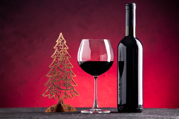 Bicchiere da vino vista frontale e decorazione natalizia bottiglia su sfondo rosso chiaro