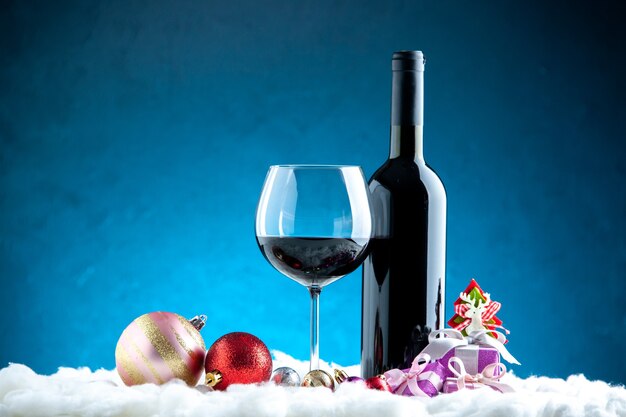 Вид спереди бокал для вина и бутылки елочные игрушки на синем фоне