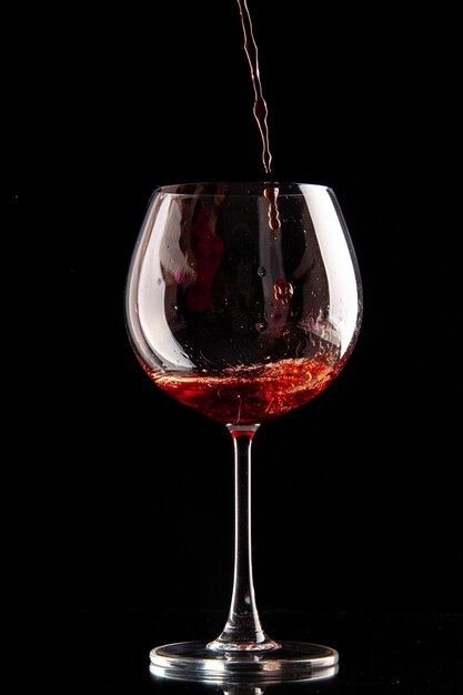 Front view wine glass getting poured with red wine on black color drink champagne alcohol
