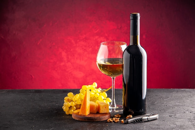 Front view wine in glass wine bottle yellow grapes cheese on wood board wine opener on dark table light red background