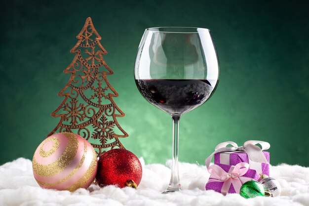 Вид спереди бокал для вина и рождественские украшения маленькие подарки на зеленом фоне