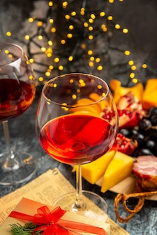 正面図ワイングラスブドウチーズピース肉スライス暗いクリスマスライトの木のプレート