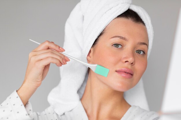 Front view of woman in bathrobe applying skincare
