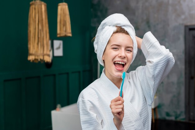 Front view of woman in bathrobe singing in toothbrush