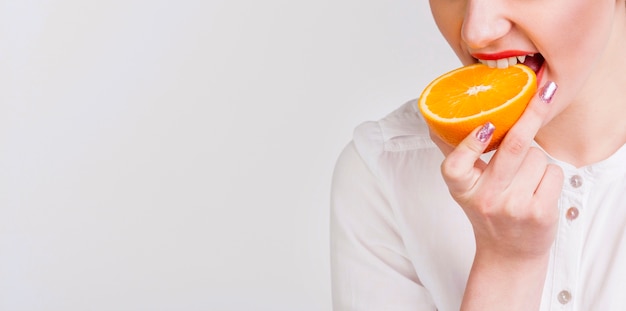 Front view of woman biting an orange