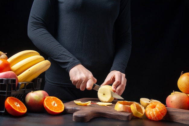 キッチンテーブルの木製トレイに木の板の果物に新鮮なリンゴを刻んでいる女性の正面図