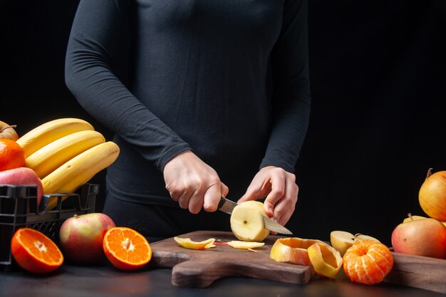 식탁에 있는 나무 쟁반에 있는 나무 판자 과일에 신선한 사과를 자르는 여성의 전면 모습