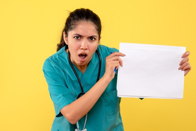 Вид спереди женщины-врача с открытым ртом, показывая документы на желтой стене