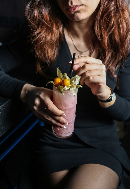 Front view woman drinking milkshake with physalis and straw