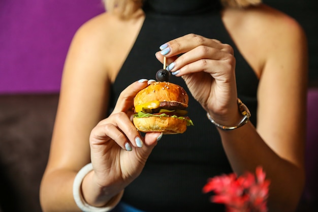 Front view woman eating mini burger with olive