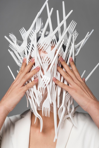 Front view woman face being covered in white plastic forks