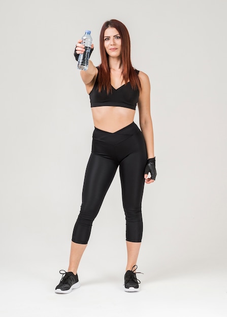 Front view of woman in gym attire posing while holding up a bottle of water