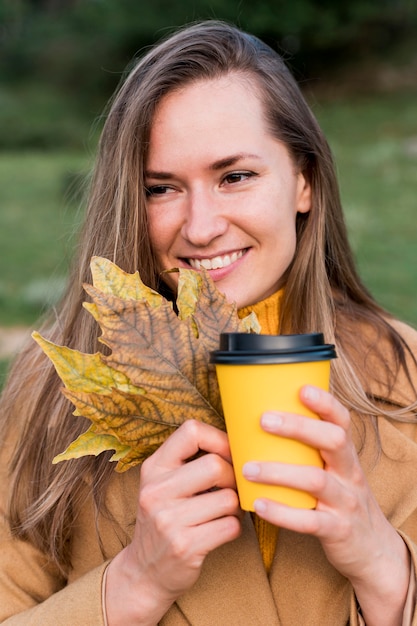 front view woman holding autumn leaves and a cup of coffee