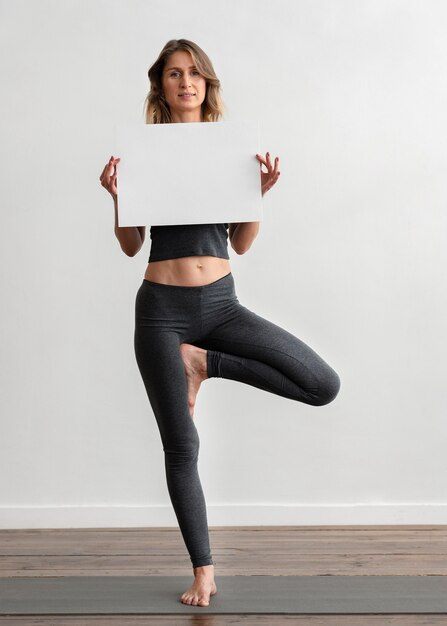 Front view of woman holding blank placard while doing yoga at home