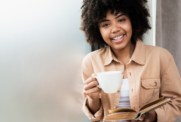 Donna di vista frontale che tiene una tazza di caffè e un libro