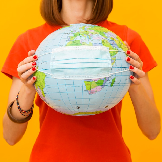 Front view of woman holding globe with medical mask