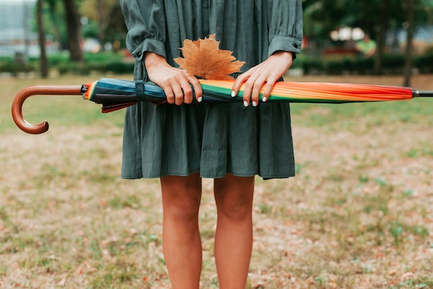 Foto gratuita donna di vista frontale che tiene foglie e un ombrello colorato