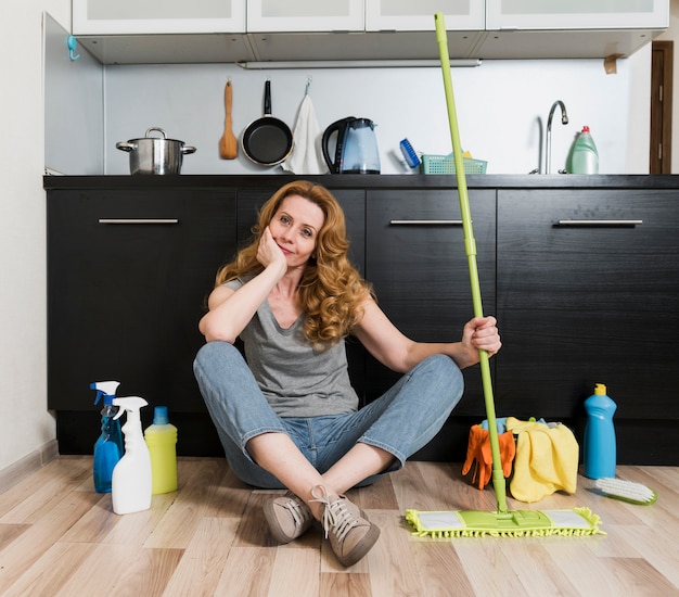 Front view of woman holding mop with cleaning products