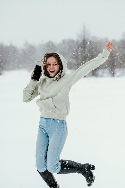 Front view of woman holding smartphone and jumping in the air outdoors