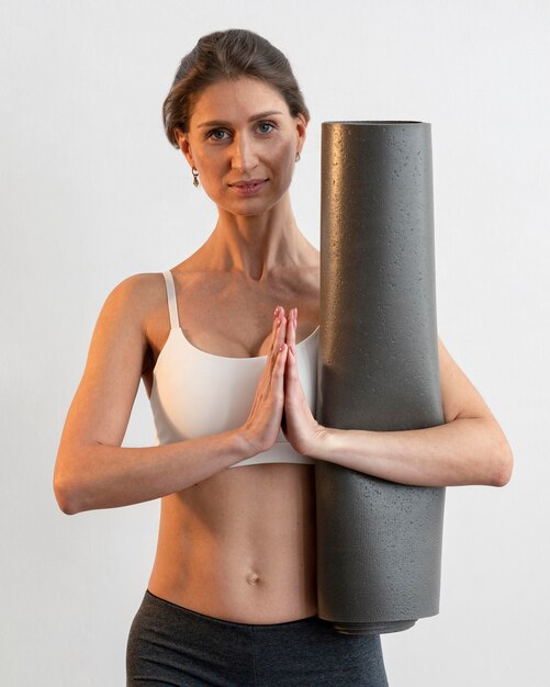 Front view of woman holding yoga mat while doing a pose