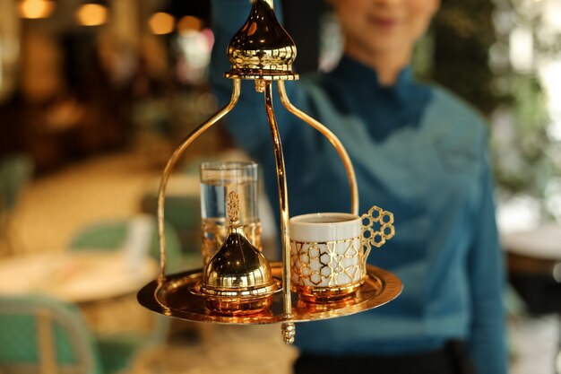 Front view woman holds a tray with turkish coffee and turkish delight with a glass of water