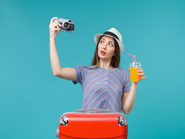 無料写真 青い背景の海の航海夏の旅行の旅の休暇でジュースとカメラを保持している休暇中の正面図の女性