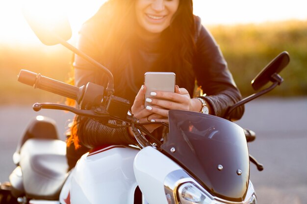 Вид спереди женщины, смотрящей на смартфон, сидя на мотоцикле