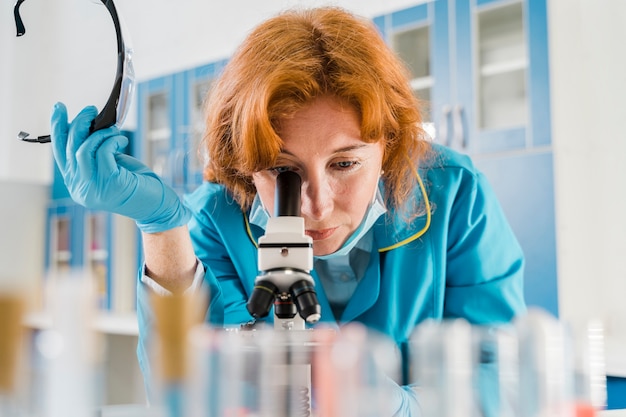 Женщина вид спереди смотрит в микроскоп