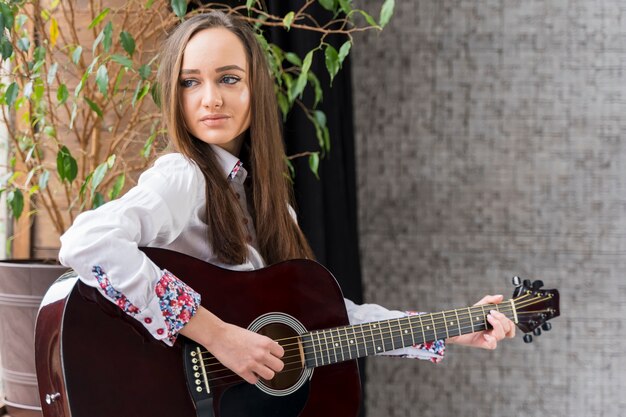 Front view woman playing chords on guitar and looking away