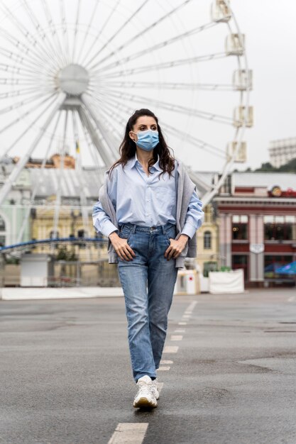 Front view woman posing in an amusement park while wearing a medical mask