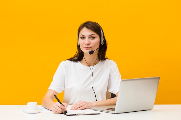 Foto gratuita vista frontale della donna che posa alla sua scrivania mentre indossa l'auricolare