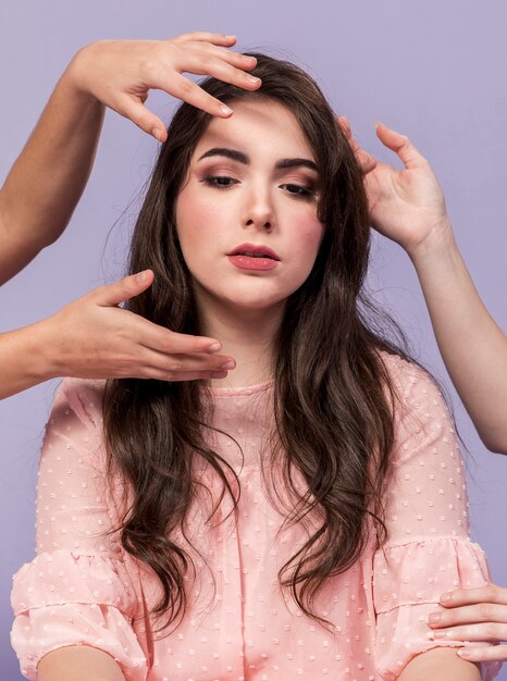 Front view of woman posing other women's hands around her head