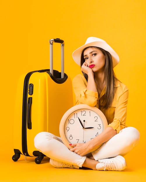 Foto gratuita vista frontale della donna che posa tenendo l'orologio accanto ai bagagli