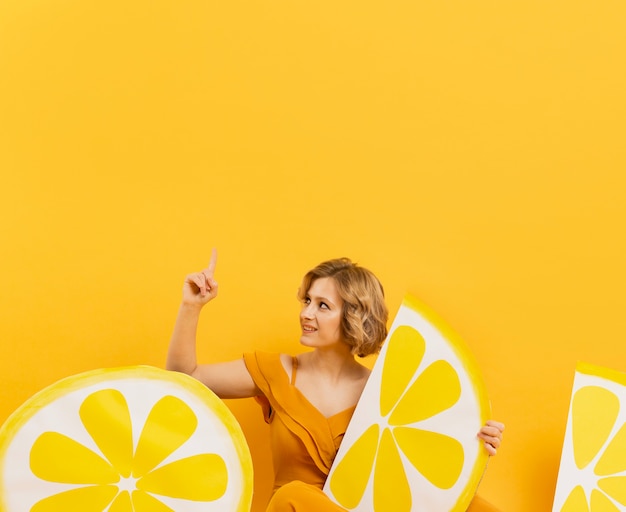 Free photo front view of woman posing with lemon slices decor and pointing up