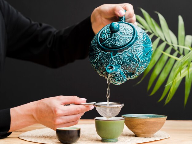 Front view woman pouring tea in teacup using strainer