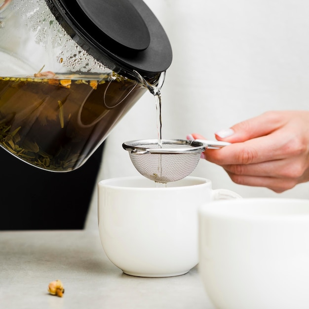 Front view woman pouring tea through strainer