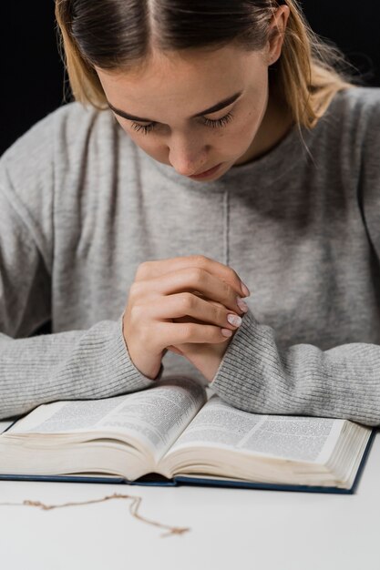 Вид спереди женщины, молящейся и читающей из библии