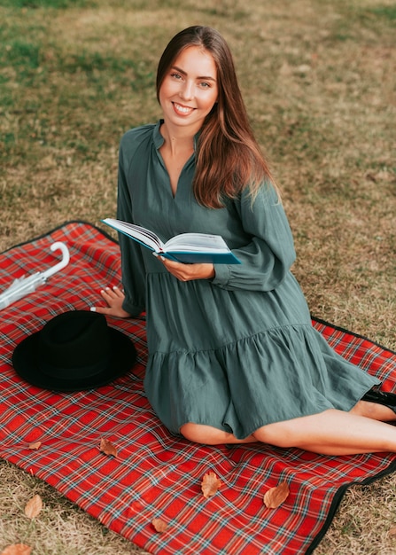 Donna di vista frontale che legge un libro su una coperta da picnic