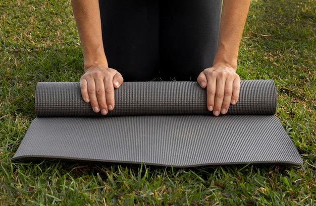 Front view of woman rolling yoga mat on the grass