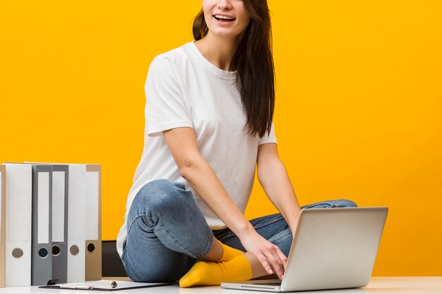 Front view of woman sitting on desk and working on the laptop while smiling