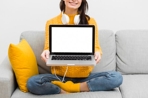 Front view of woman sitting on sofa showing her laptop