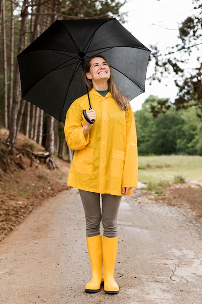 Free photo front view woman standing in the forest while holding an umbrella