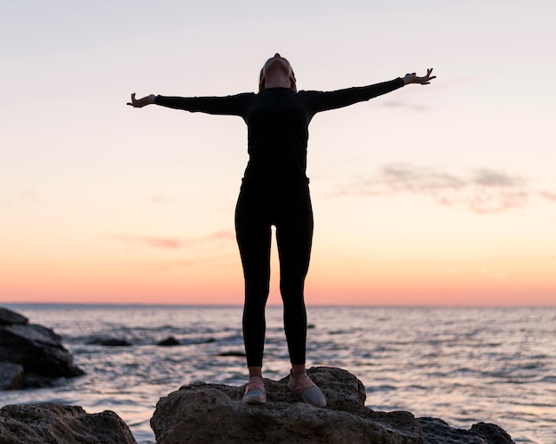 Front view woman standing on rocks next to the ocean