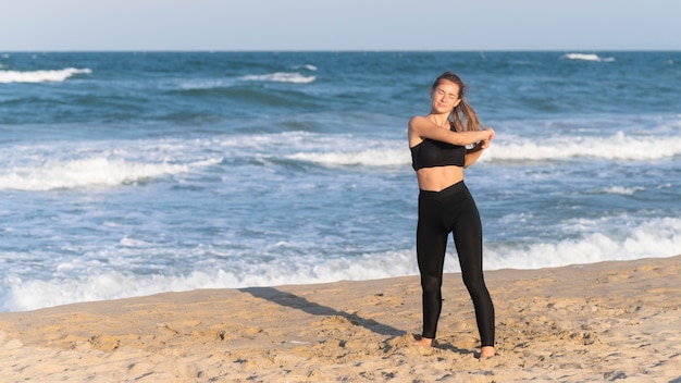 Foto gratuita vista frontale della donna che allunga prima di esercitare sulla spiaggia