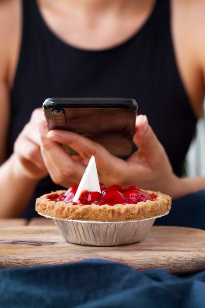 Front view of woman taking photo of fruit tart with smartphone