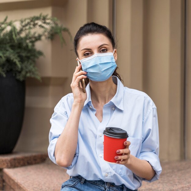 Front view woman talking on the phone with a medical mask on