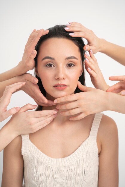 Front view of woman in tank top posing for minimalistic portrait with other women's hands close to her face