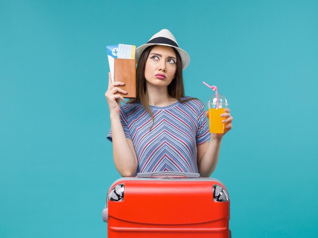 Front view woman in vacation holding fresh juice and tickets on light blue background trip journey voyage vacation sea summer