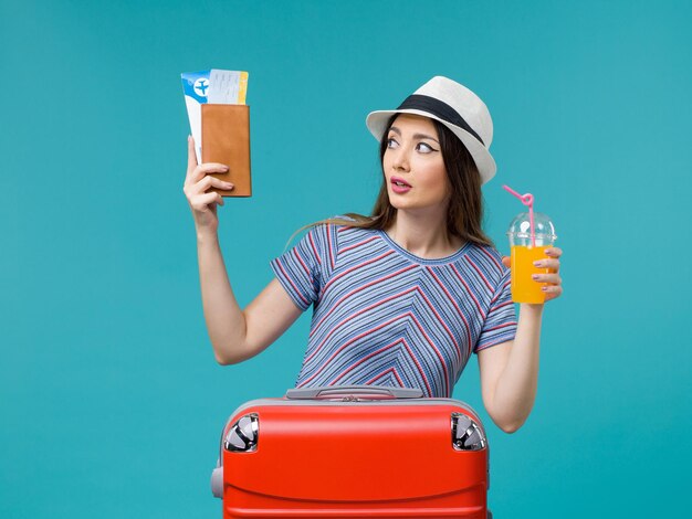 Front view woman in vacation holding her juice and tickets on light blue background trip summer sea journey voyage vacation